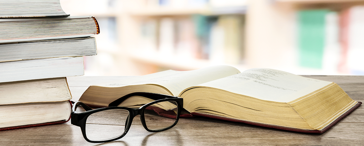 Paire de lunettes sur un bureau situÃ©e Ã  cÃ´tÃ© dâ€™une pile de livres.